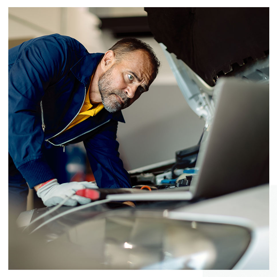Un electrician din Sibiu care prestează servicii uitându-se la un laptop sub capota unei mașini.